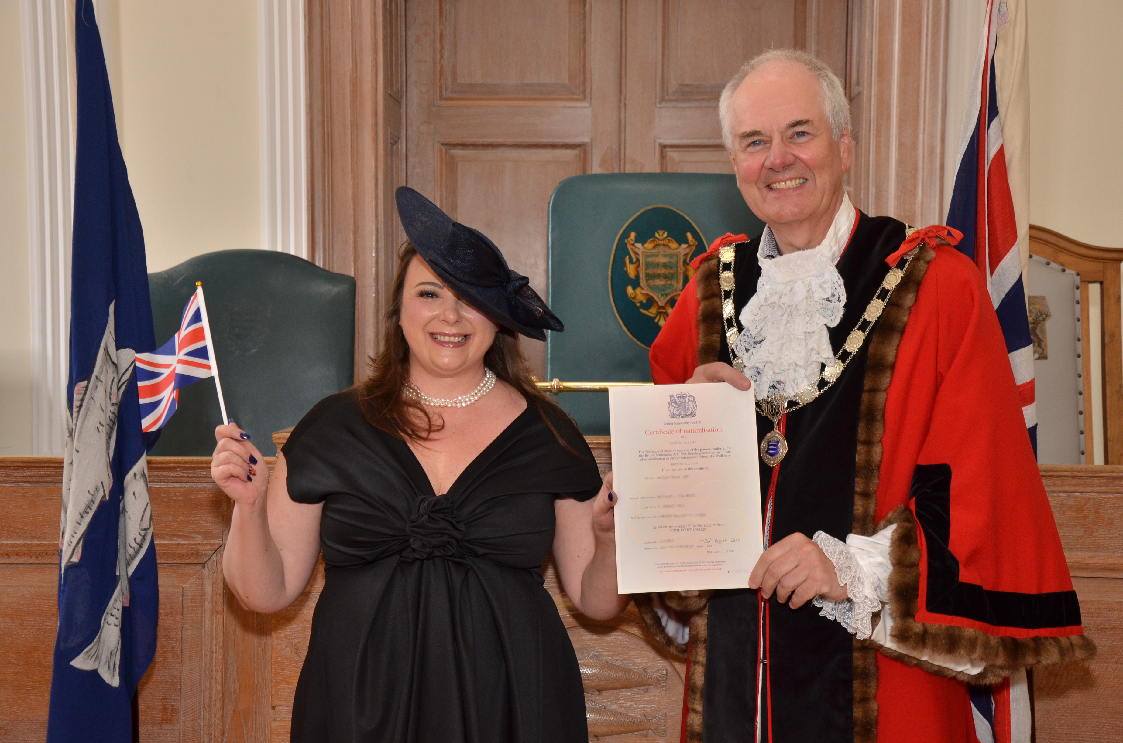well dressed female holding small Union Jack receiving certificate from male dressed in mayoral attire