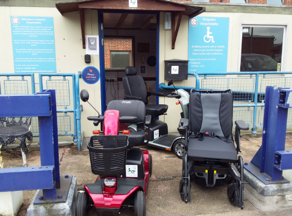 Three motorised wheelchairs outside a building displaying shopmobility signage