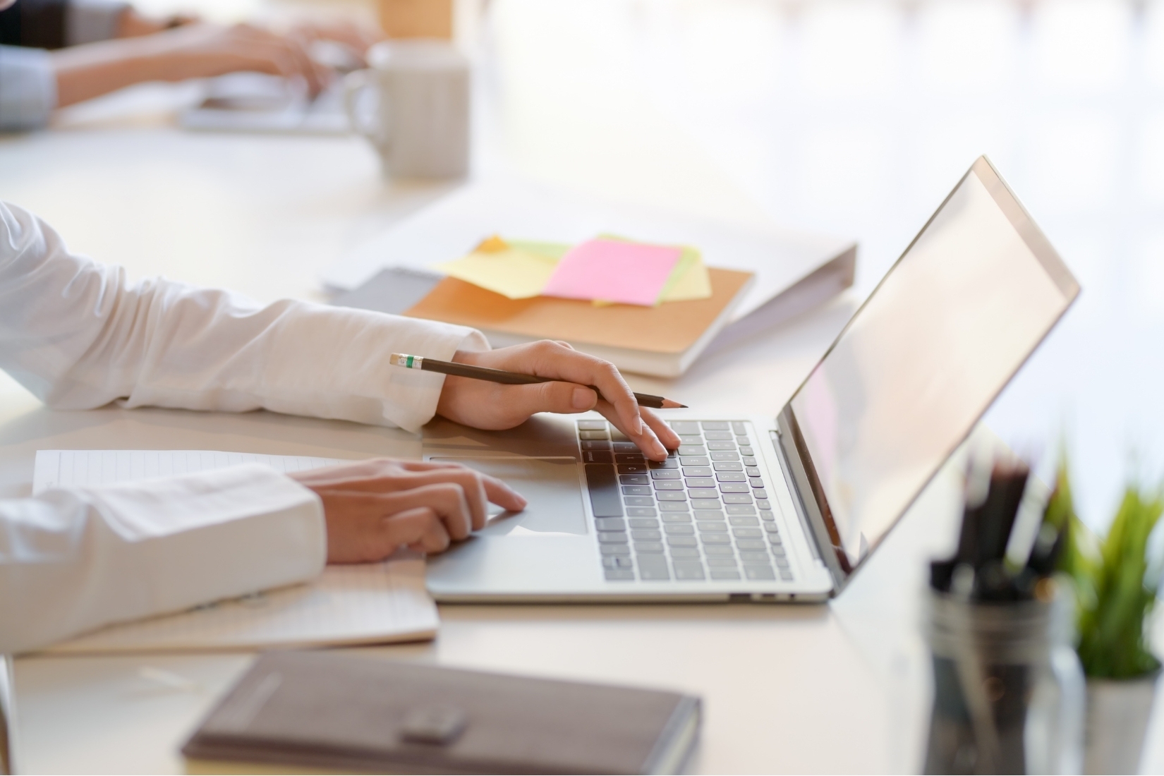 Close up of someone working at a laptop on an office desk. We see only the person's arms as they use the laptop.