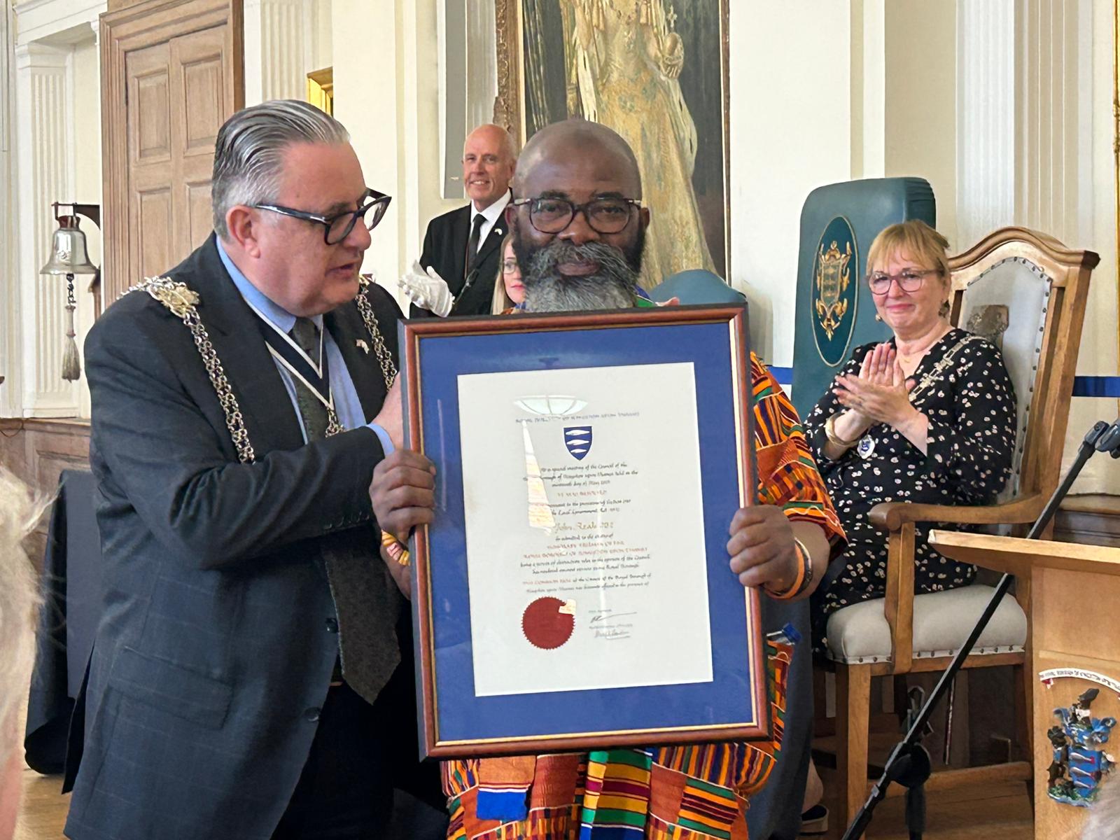 John Azah being made an Honorary Freeman of the borough. He is being presented a framed certificate by the Mayor of Kingston, Councillor Noel Hadjimichael