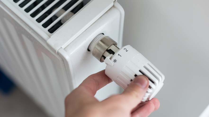 Close up of a hand turning the temperature control on a radiator