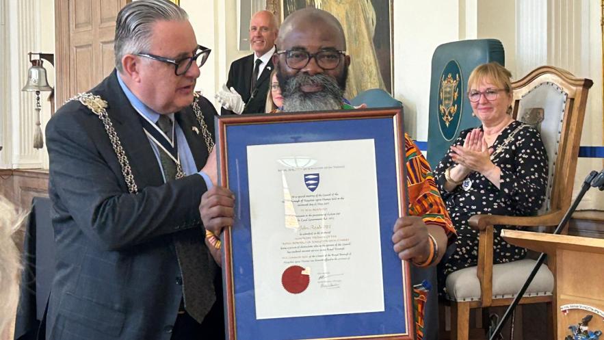 John Azah being made an Honorary Freeman of the borough. He is being presented a framed certificate by the Mayor of Kingston, Councillor Noel Hadjimichael